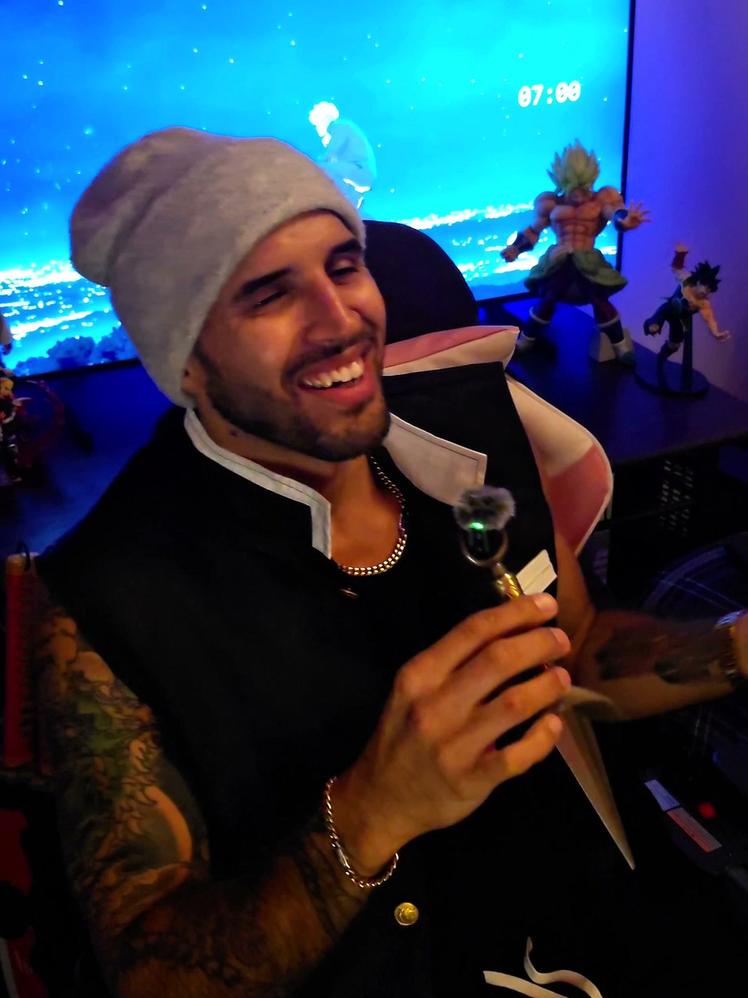 Xavier Cruz laughing in a gray beanie, anime figures and a TV behind him